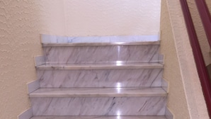 Una escalera de mármol con una pared color beige a un lado y una barandilla roja al otro.