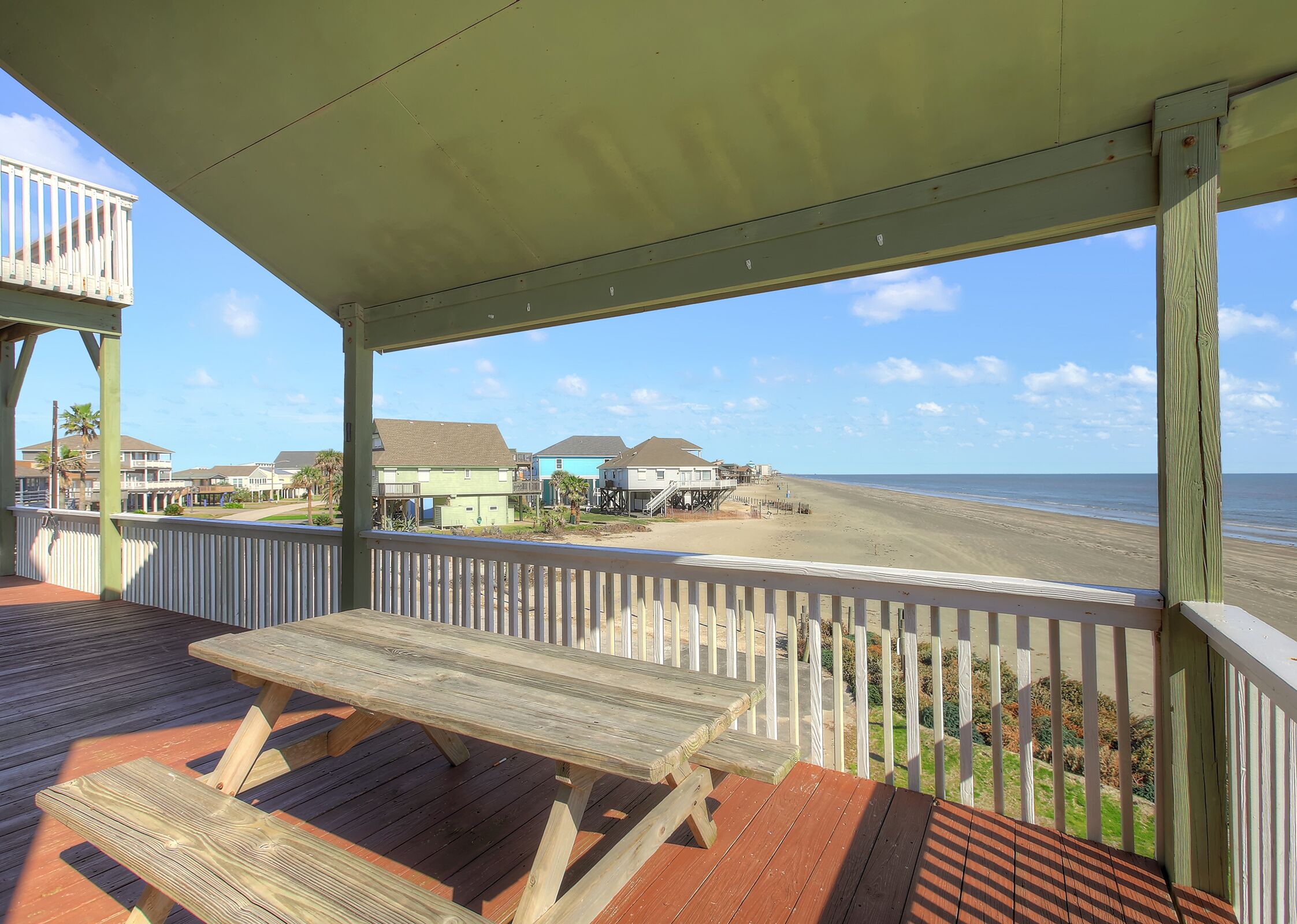 A wooden deck with picnic tables overlooking a beach with houses in the background.