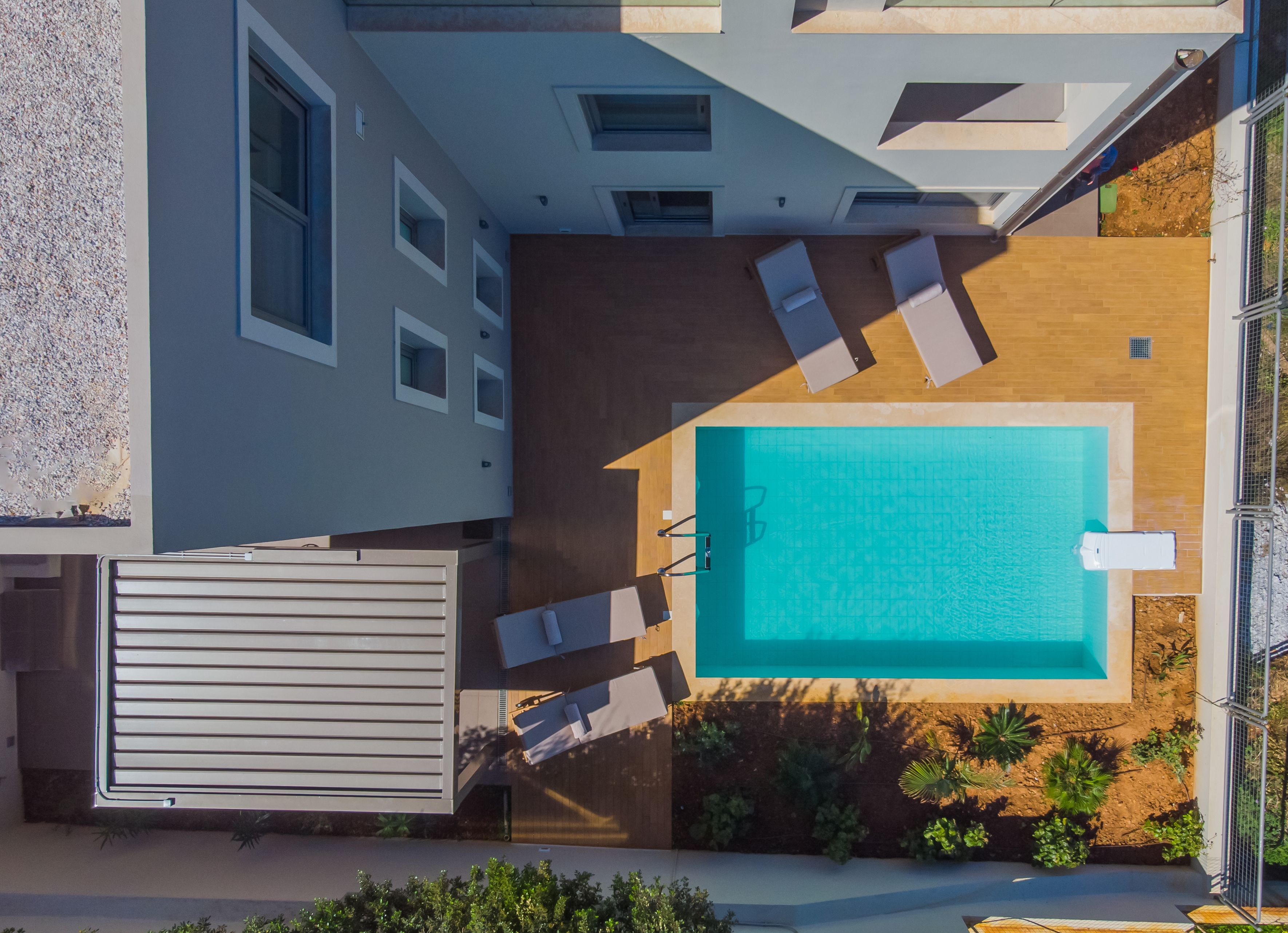 Una piscina sul tetto con un pontile in legno e poltrone relax, circondata da un edificio moderno con ampie finestre e una zona coperta.