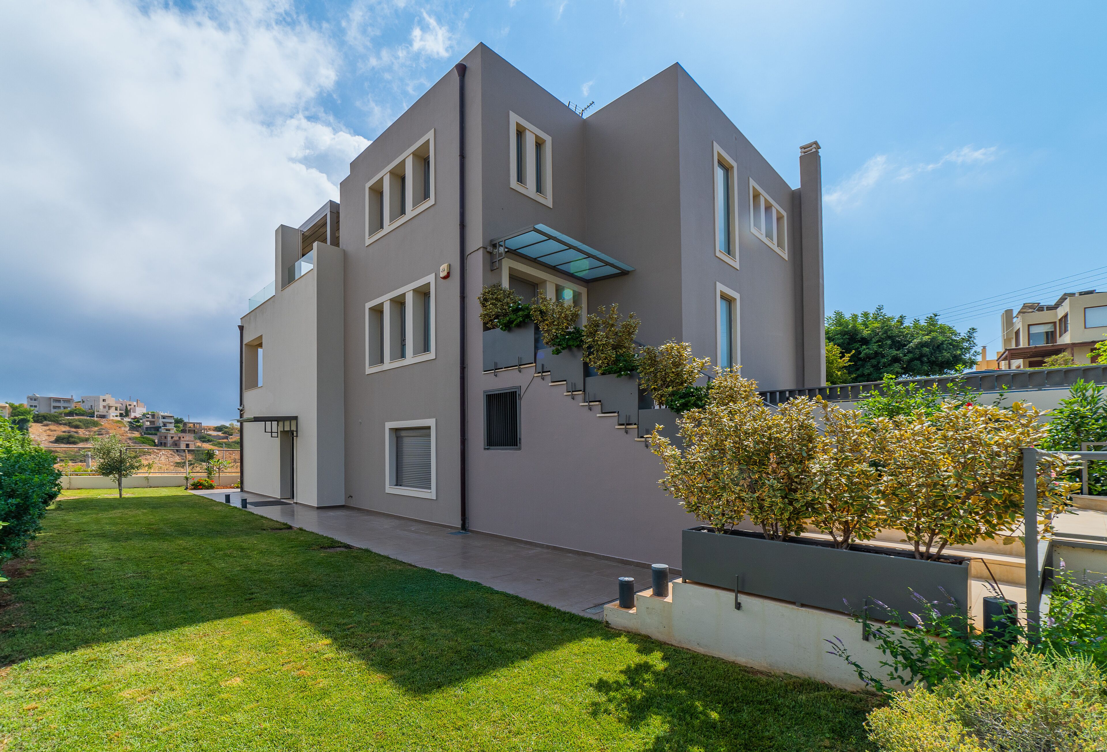 A modern two-story house with a flat roof, large windows, and a visible staircase leading to the upper floor.