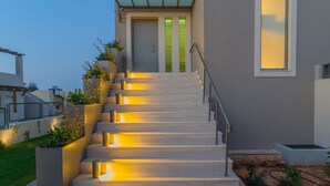 Una casa moderna amb una escala que condueix a una porta verda, envoltada de jardineres i il·luminada per una llum càlida.