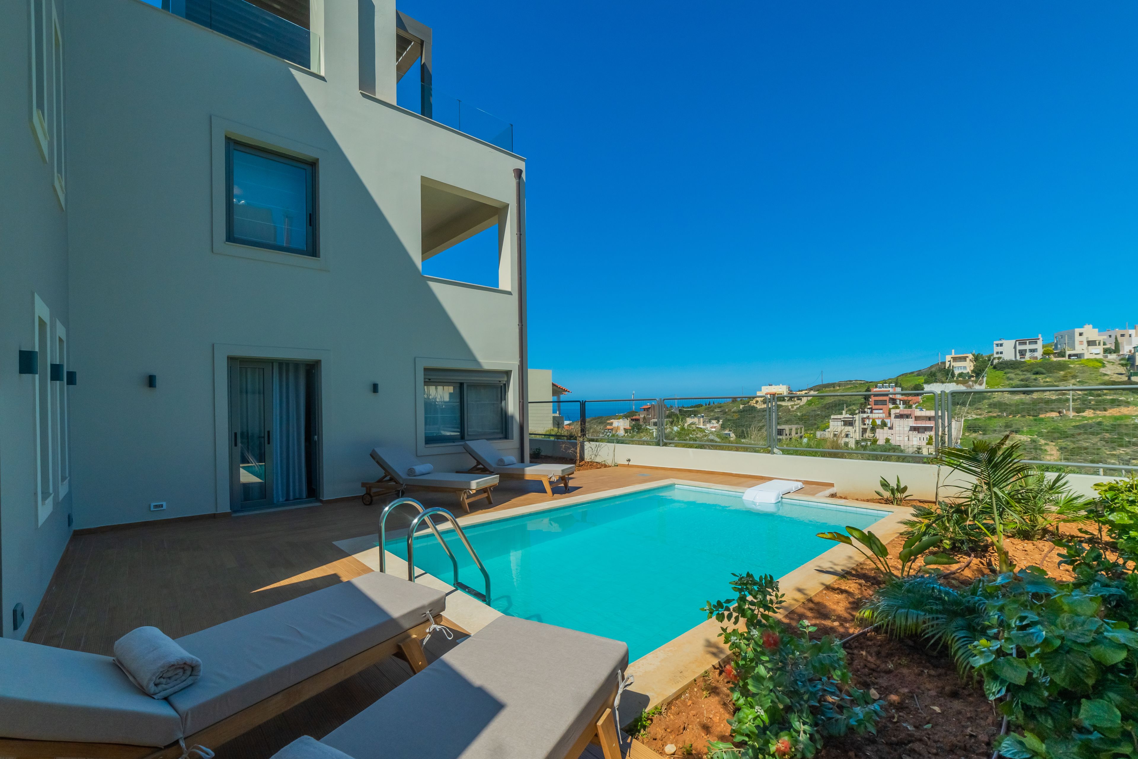 Un edificio moderno con piscina en la azotea, sillones de descanso y vistas a la costa.