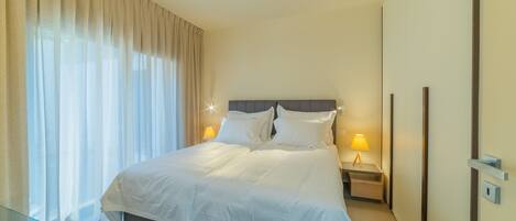 A modern hotel room with a large bed, bedside lamps, and a glass table.