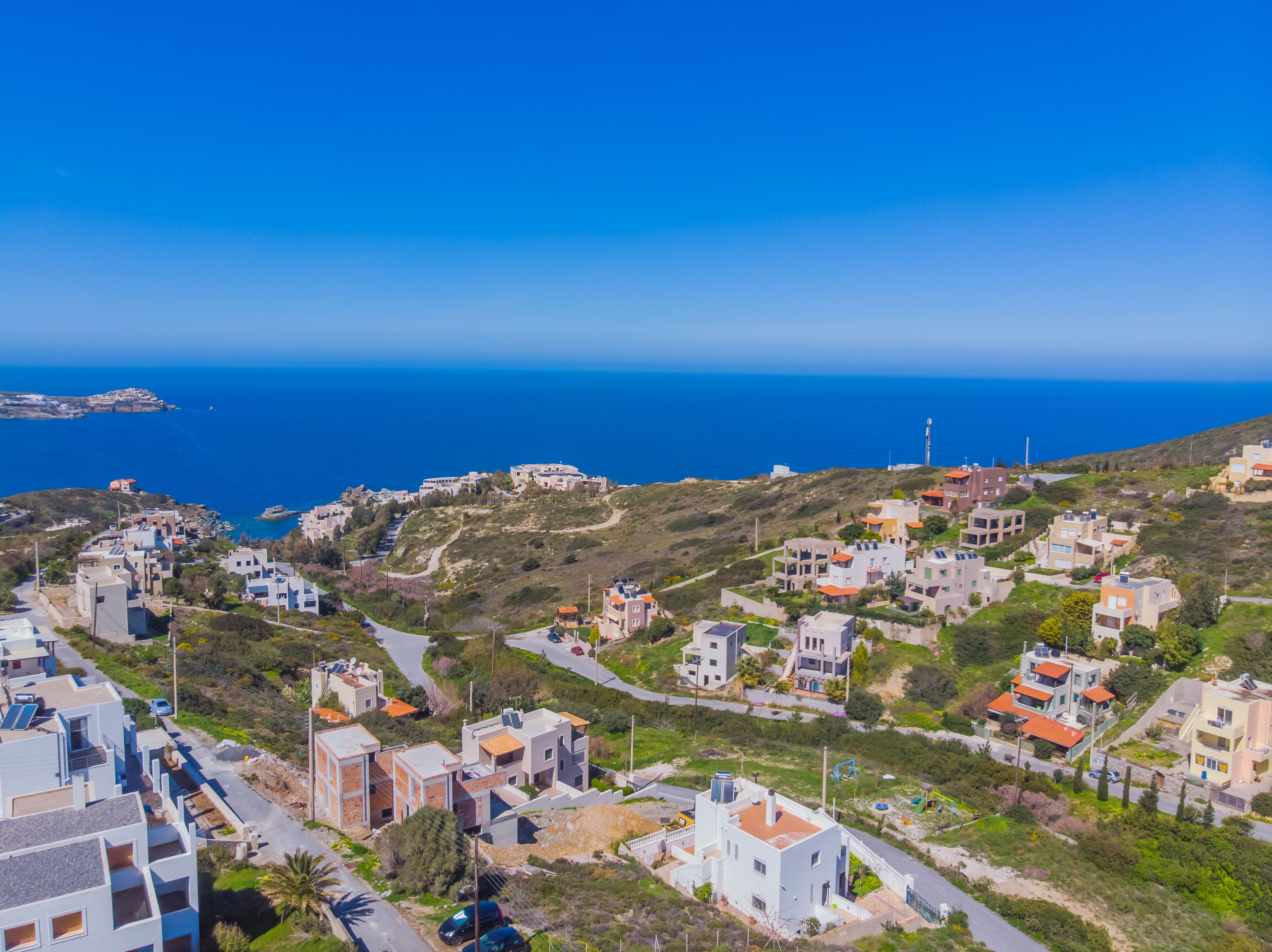 Una zona residenziale costiera con case moderne, cielo azzurro limpido e il mare sullo sfondo.