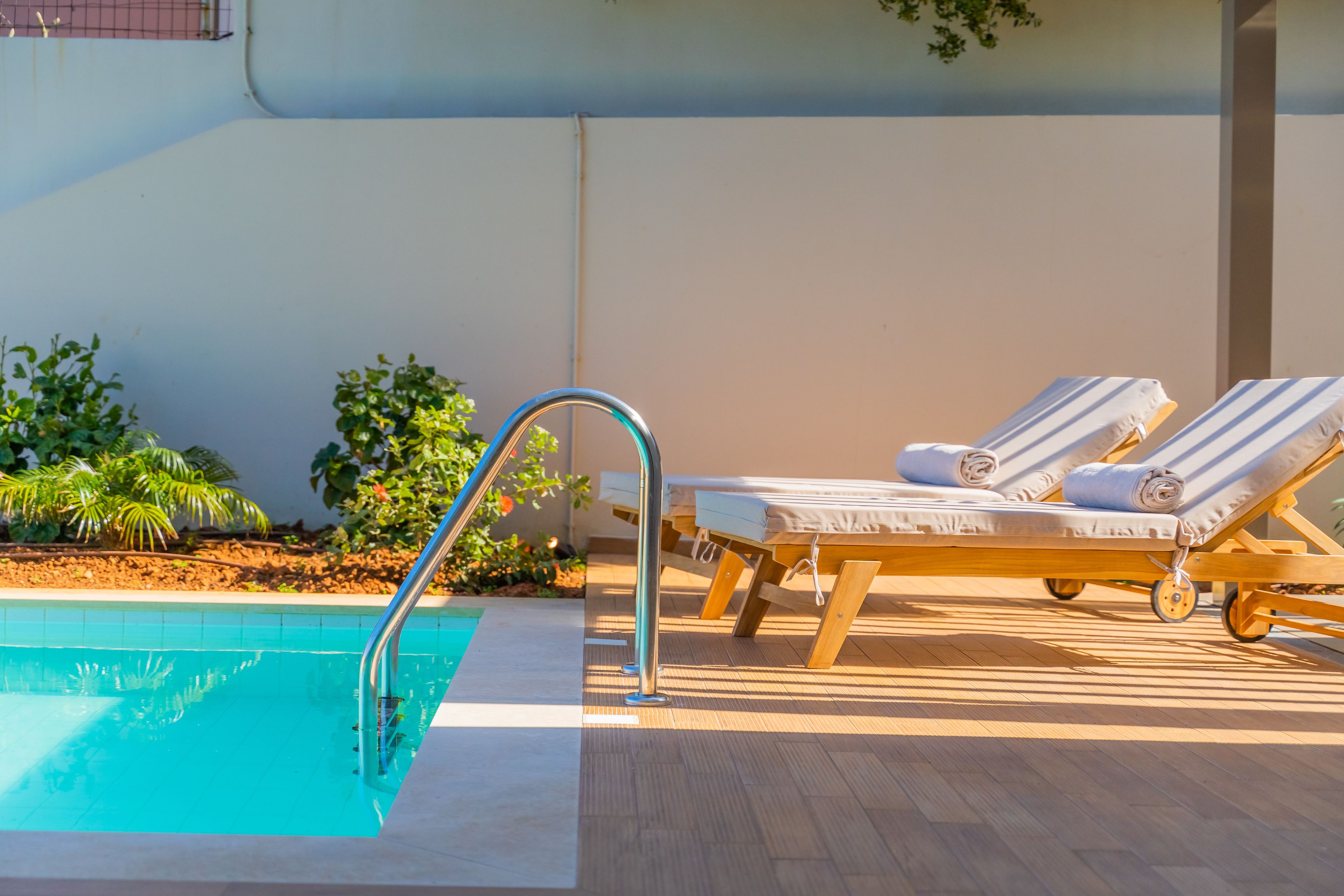 A pool area with a metal ladder, lounge chairs, and a tiled floor.