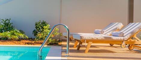 A pool area with a metal ladder, lounge chairs, and a tiled floor.