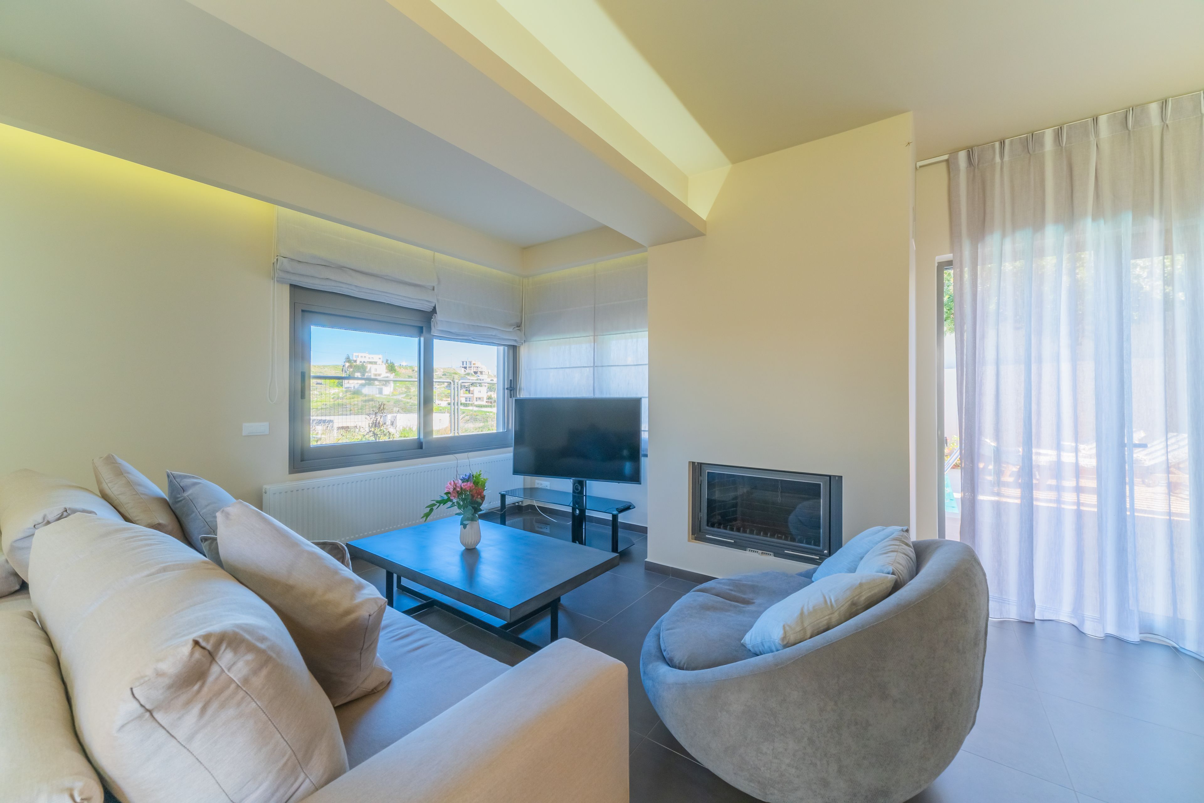 A modern living room with a sofa, armchair, TV, and fireplace.