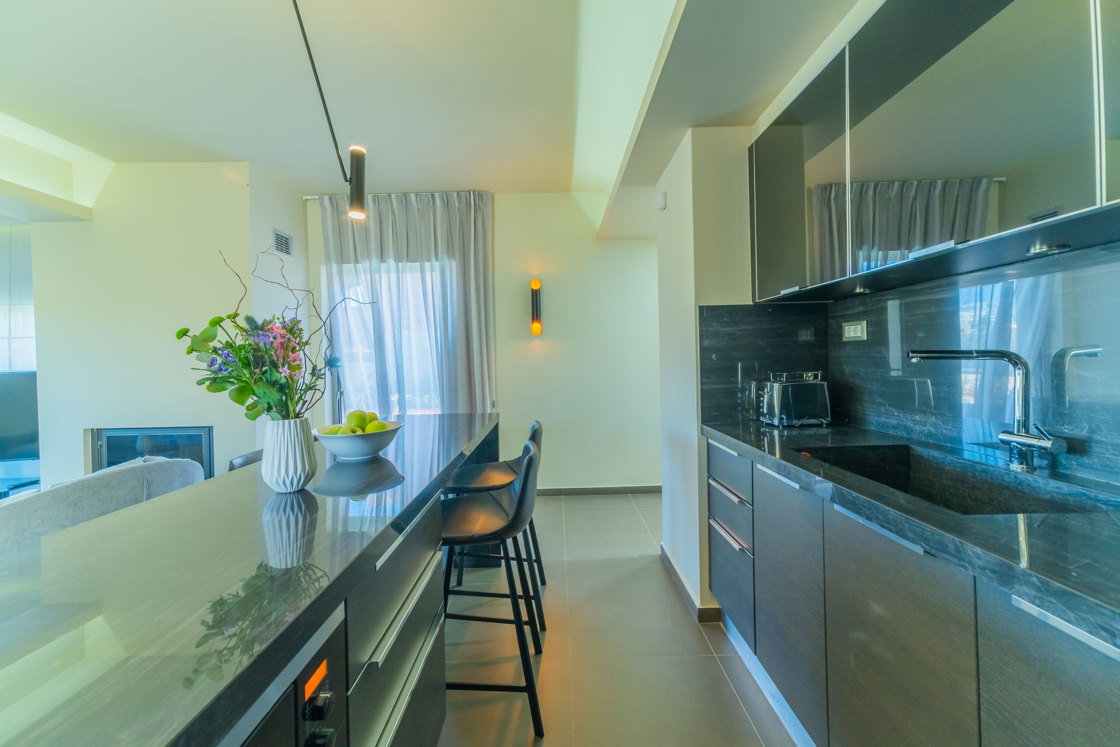 A modern kitchen with a central island, bar stools, and a vase of flowers.