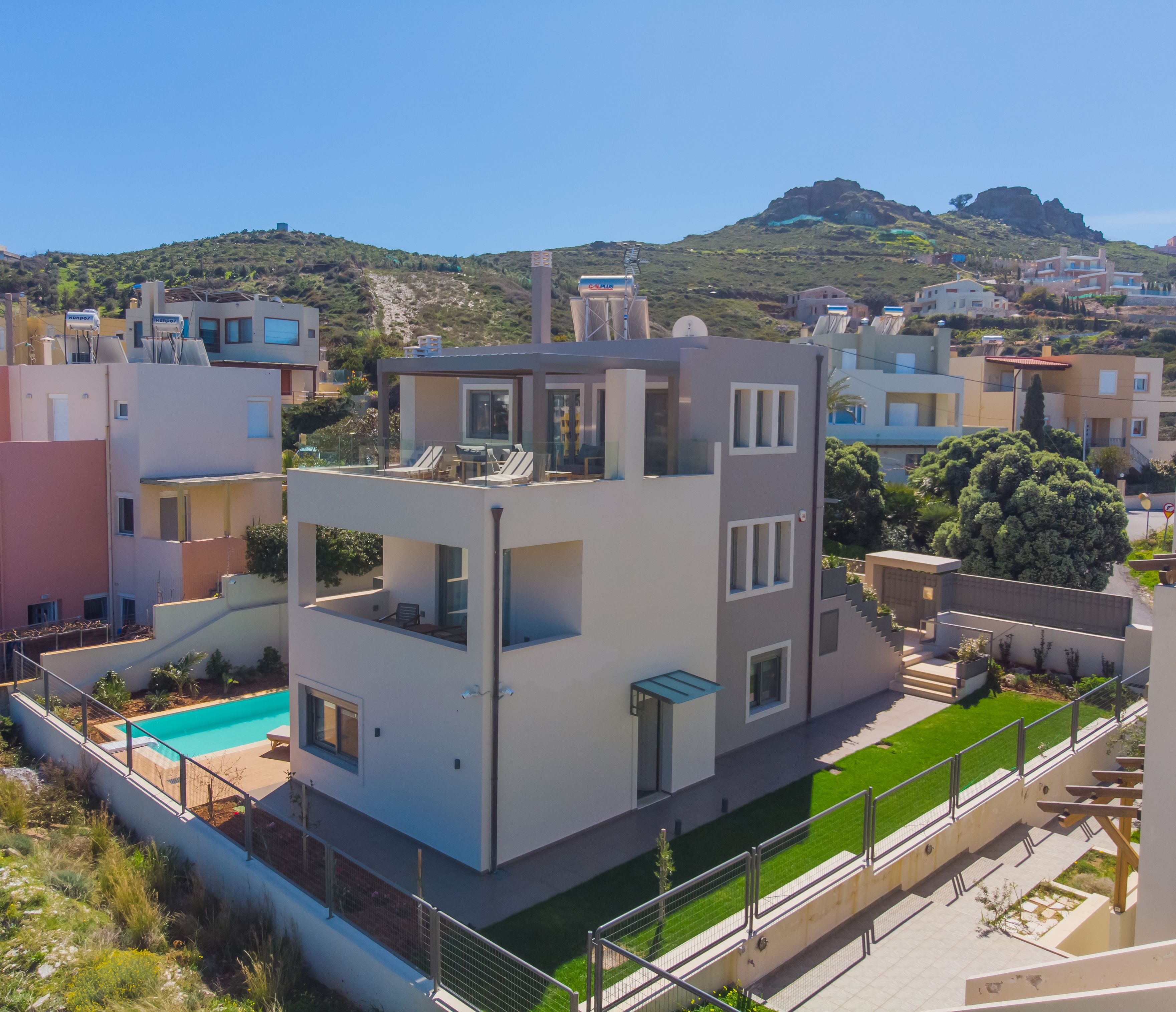A modern multi-story residential building with a rooftop pool, surrounded by greenery and a mountainous backdrop.