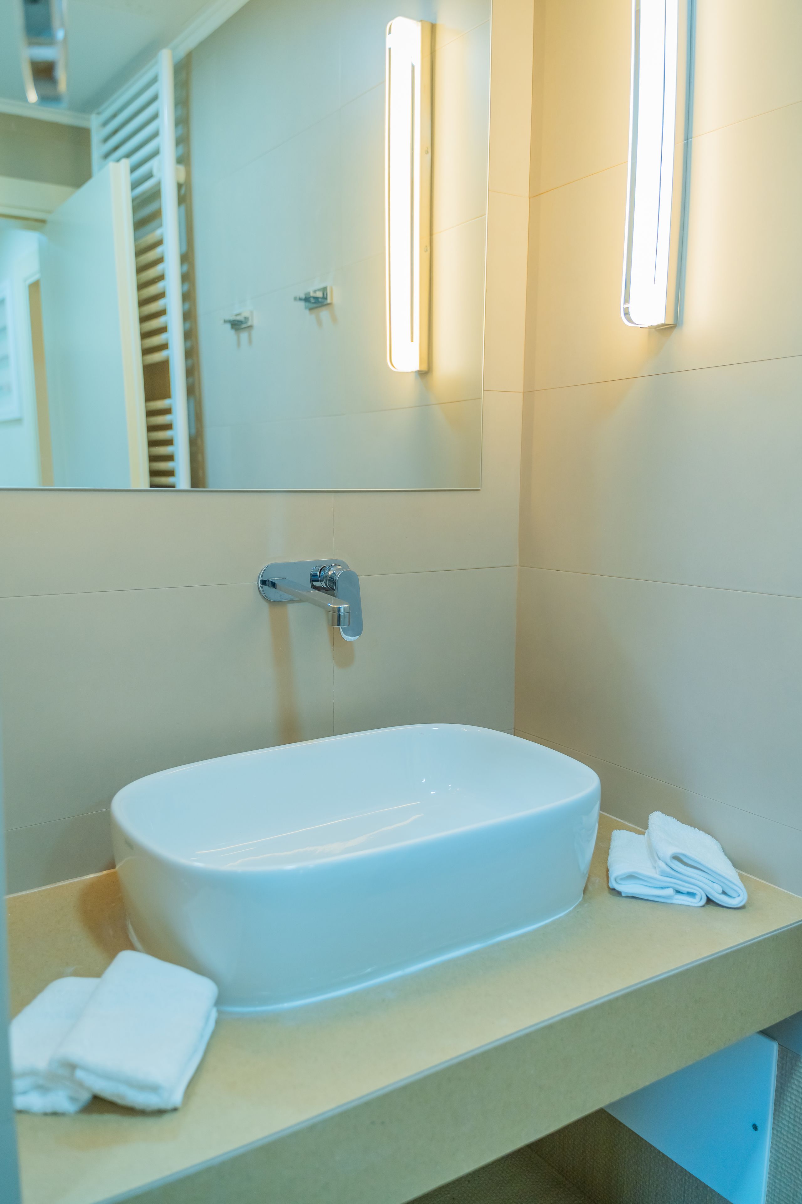 Ein modernes Badezimmer mit einem weißen Waschbecken, einem Spiegel und zwei Wandleuchten.
