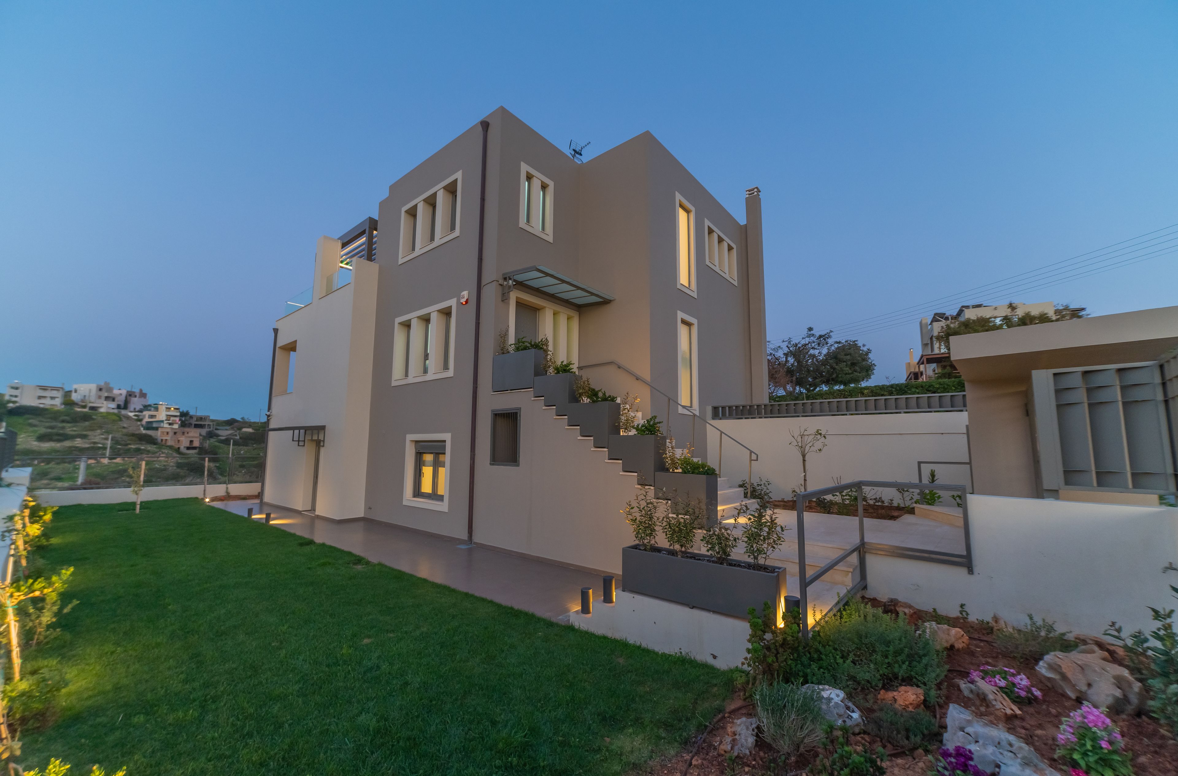 A modern two-story house with a flat roof, a central staircase, and a well-maintained lawn.