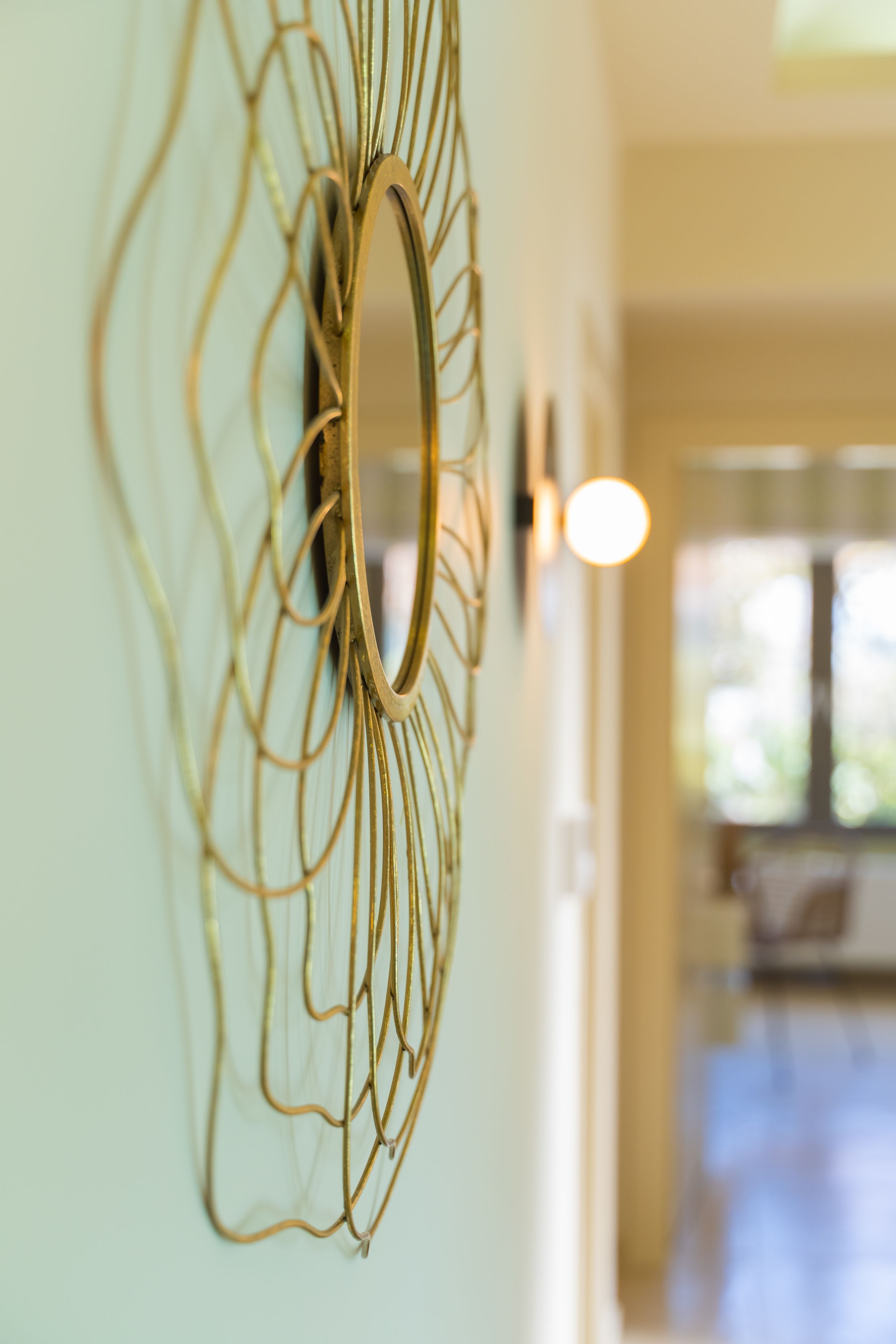 Una obra de arte abstracta dorada en la pared, con un espejo circular.