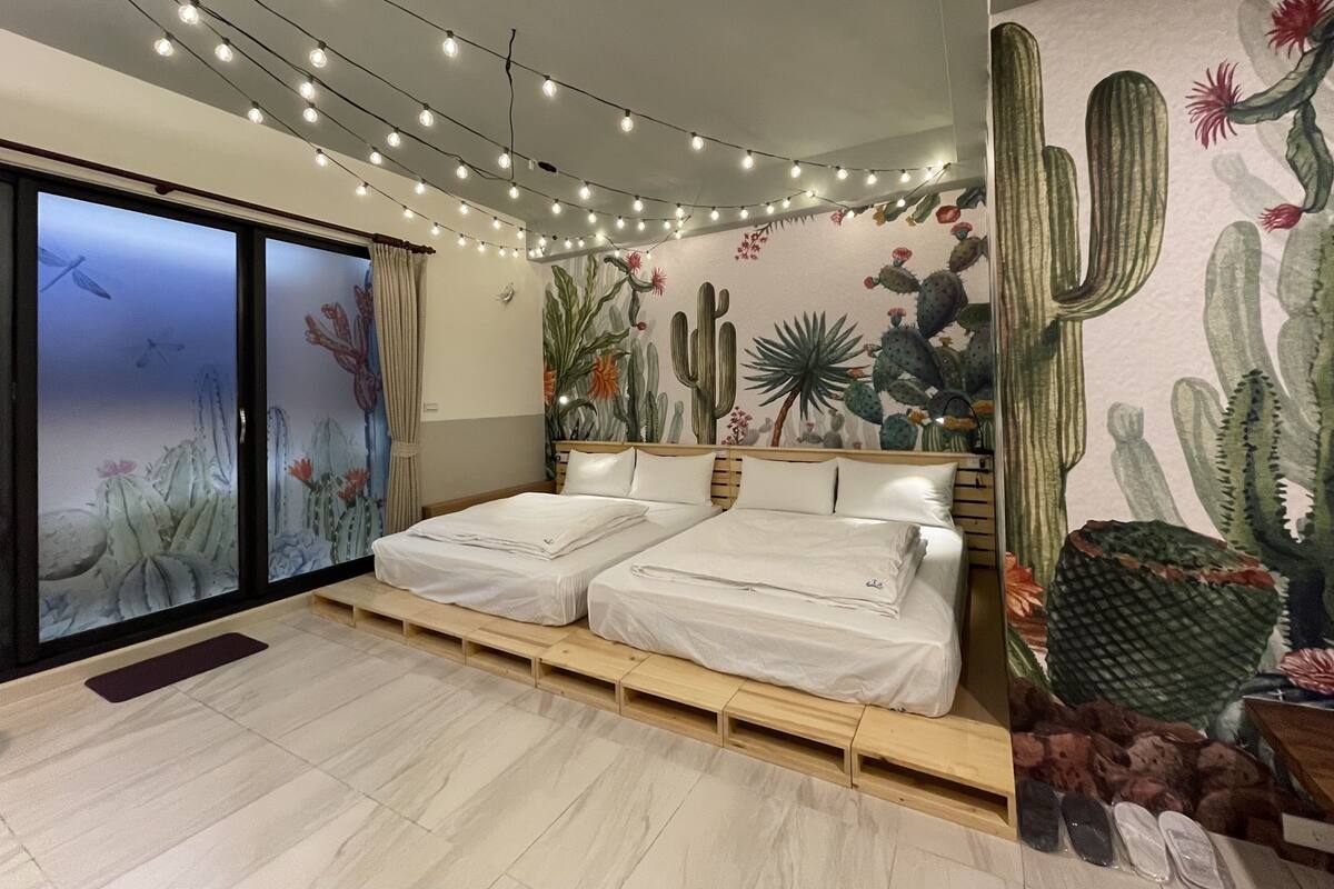 A bedroom with a double bed, a cactus mural, string lights, and a sliding glass door.