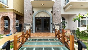 A building entrance with a wooden fence, a glass staircase, and a tiled pathway leading to a door with a decorative arch. - Yiting B&B (Checheng)
