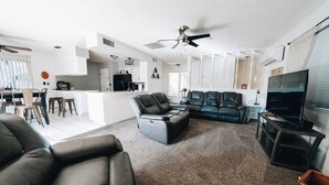 Una sala de estar moderna con un sofá modular, un televisor y un ventilador de techo.