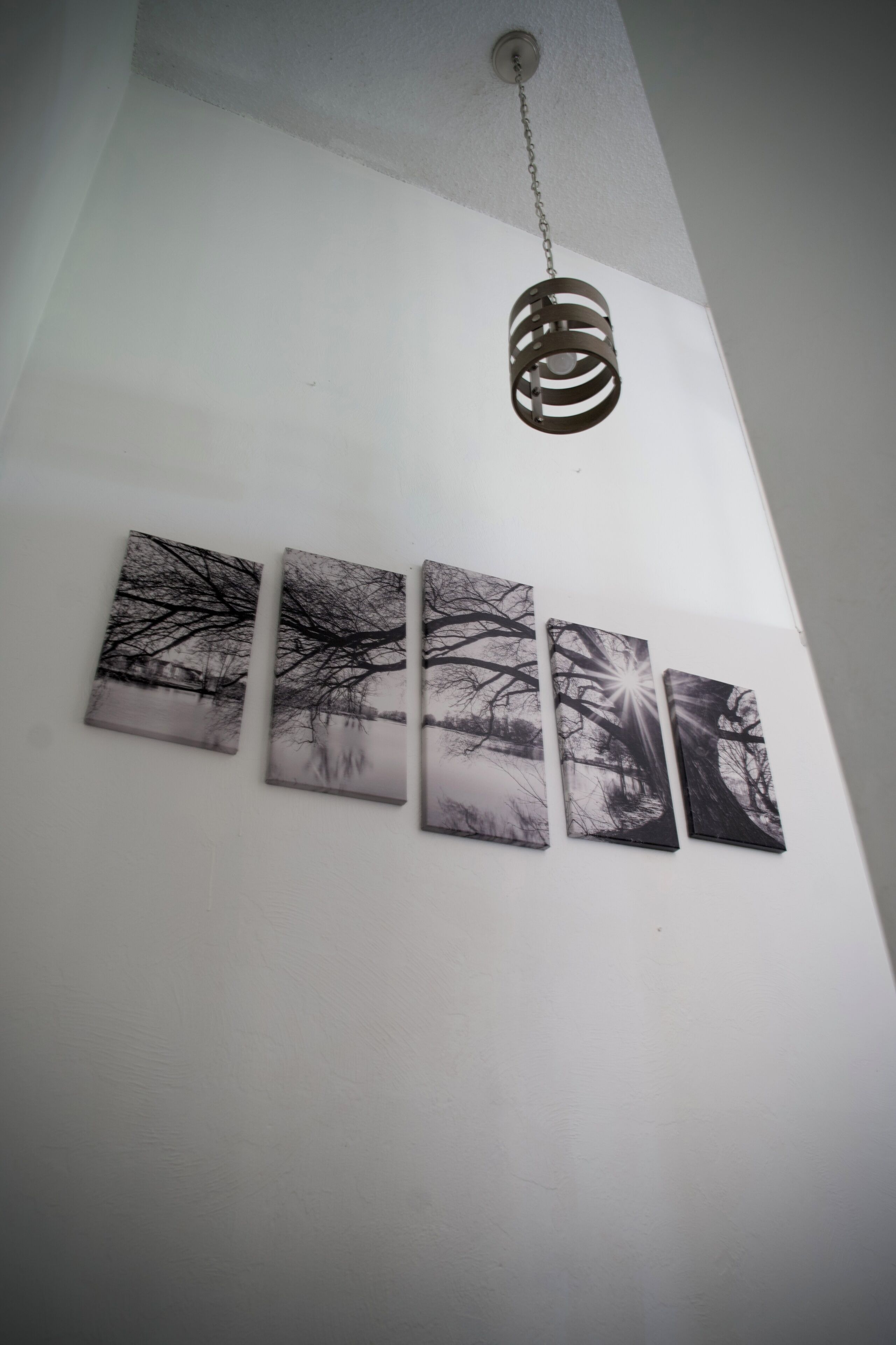 A ceiling light fixture and four black and white framed pictures on a white wall.