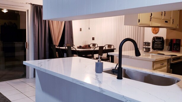Una cocina moderna con encimera de mármol, un lavabo y una zona de comedor con sillas y una mesa.