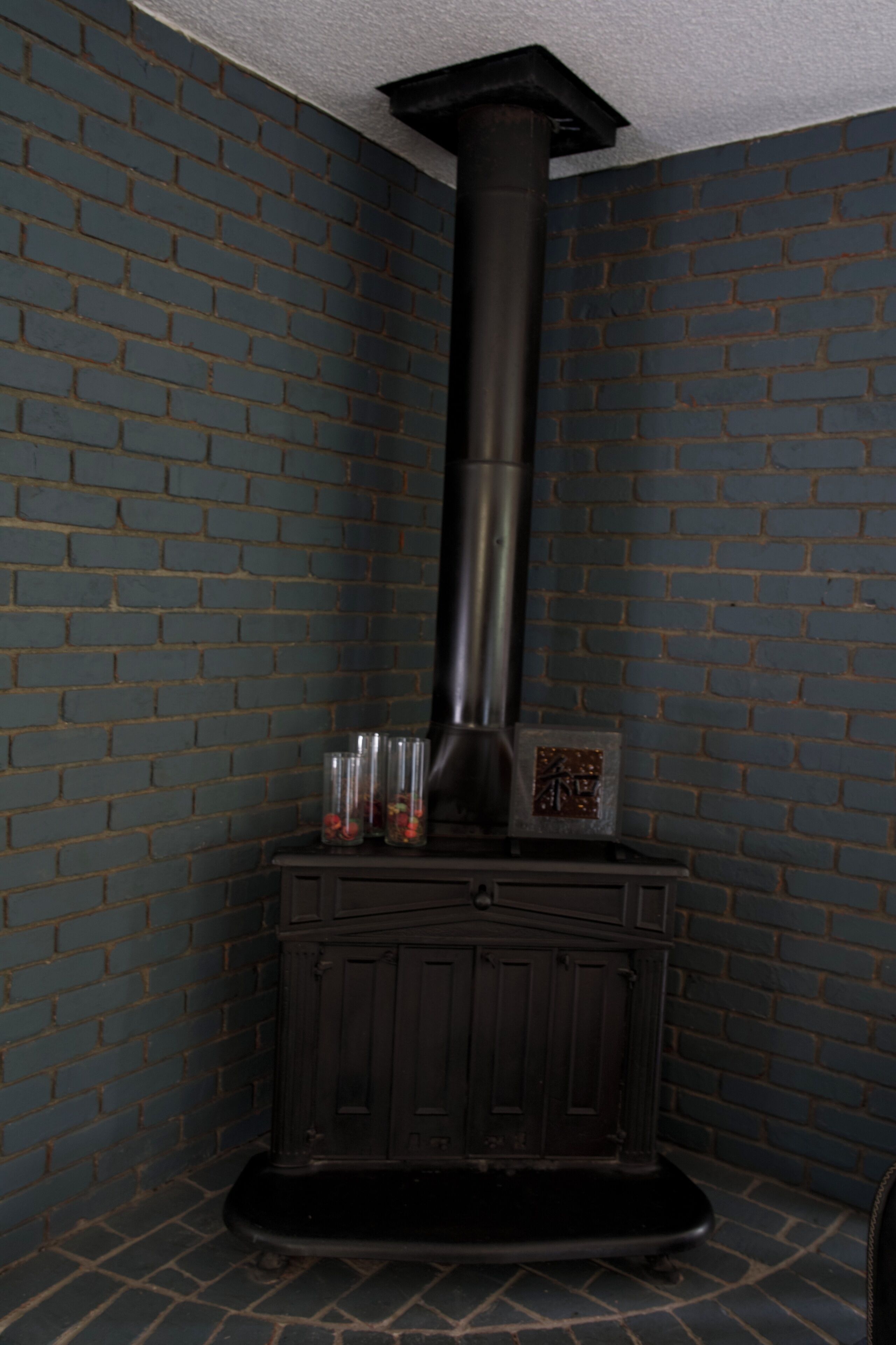 Une pièce avec un mur en briques, une cheminée noire et un meuble contenant des récipients en verre.