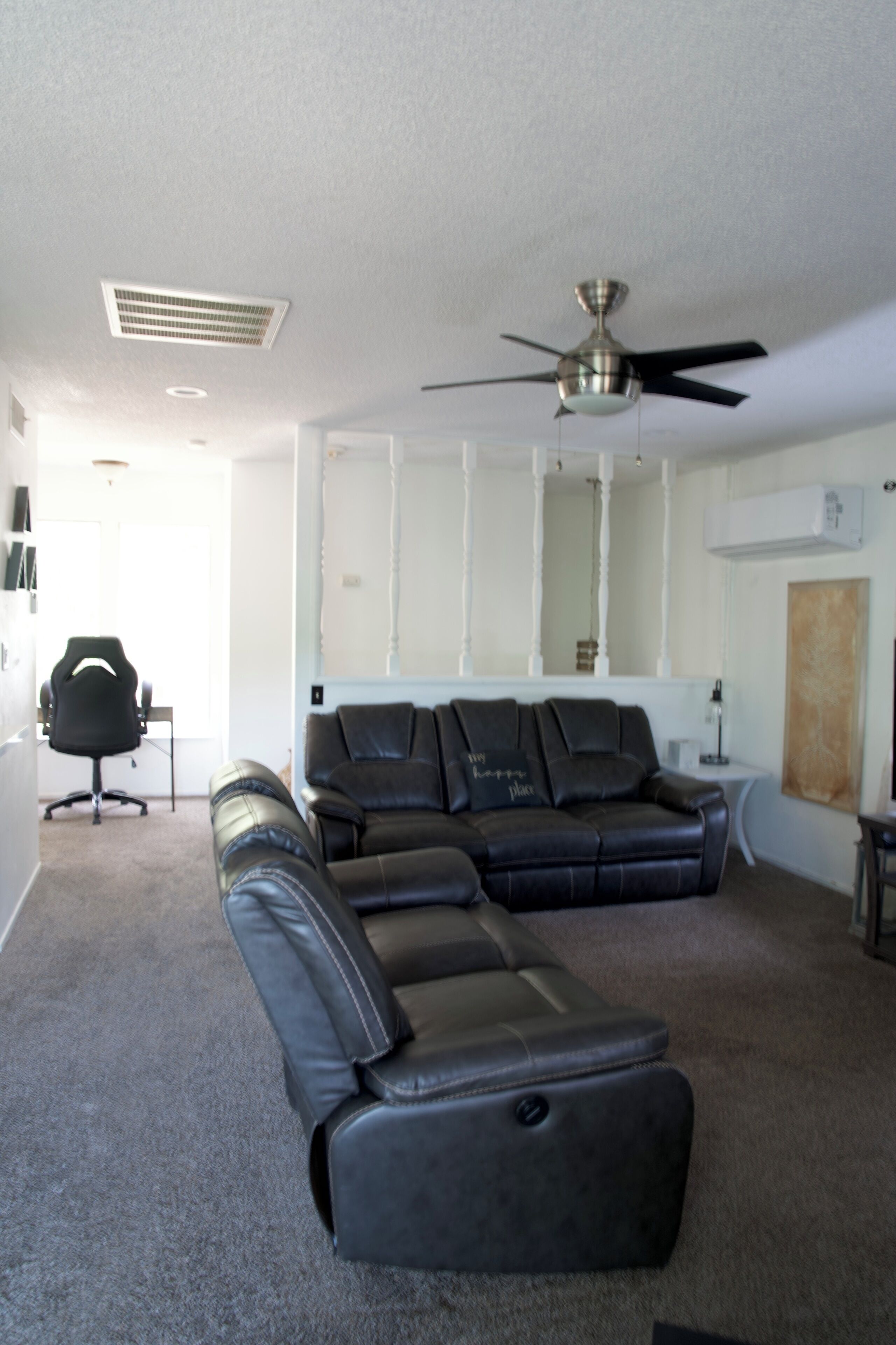 A living room with a sectional sofa, a ceiling fan, a fireplace, and a small table with a lamp.