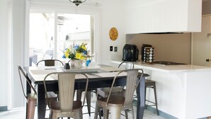 Una cocina moderna con comedor, muebles blancos, ventilador de techo y vistas al exterior.