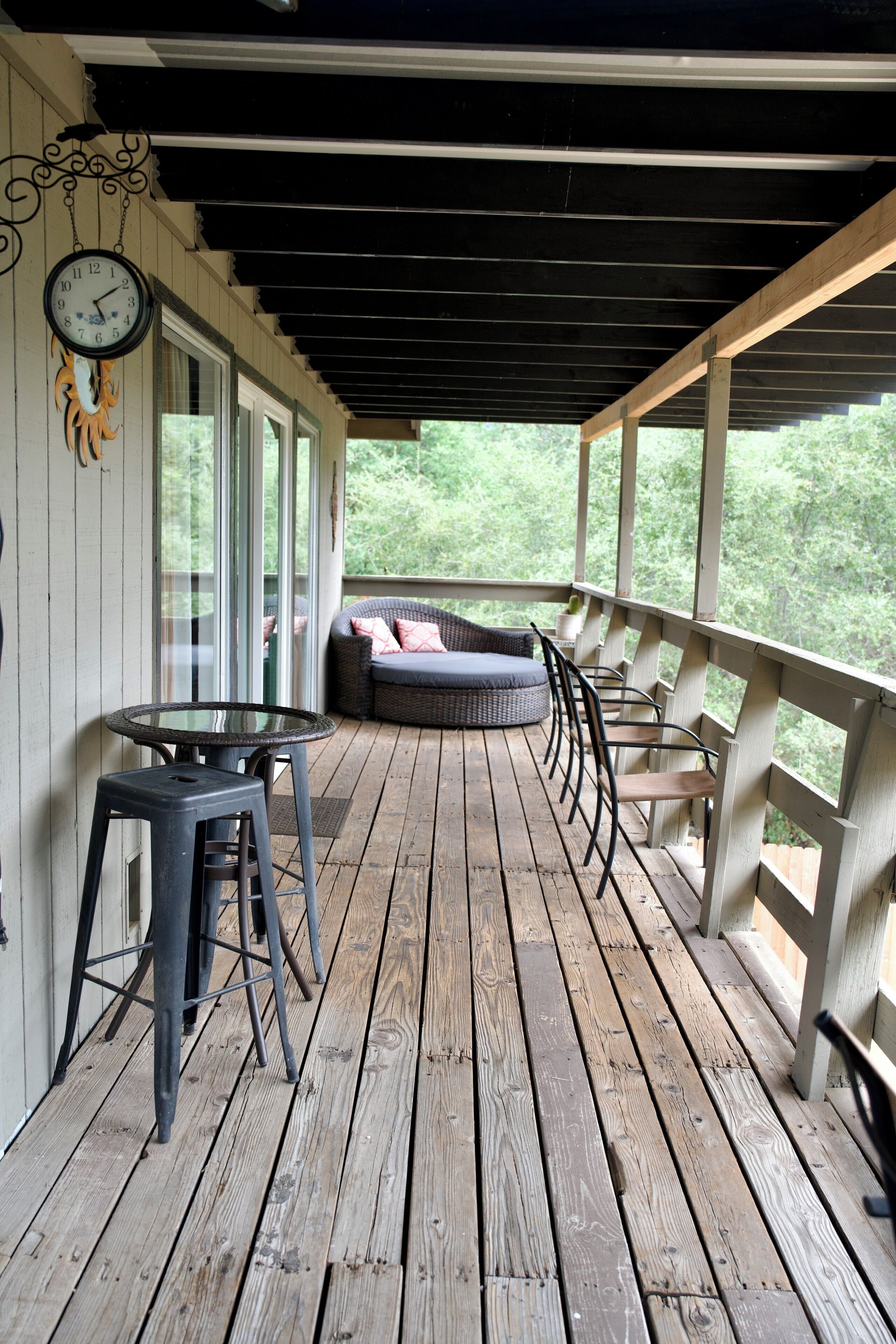A wooden deck with a glass table and chairs, a sofa, and a wall clock.