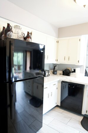 A modern kitchen with white cabinets, a black refrigerator, and a dishwasher.