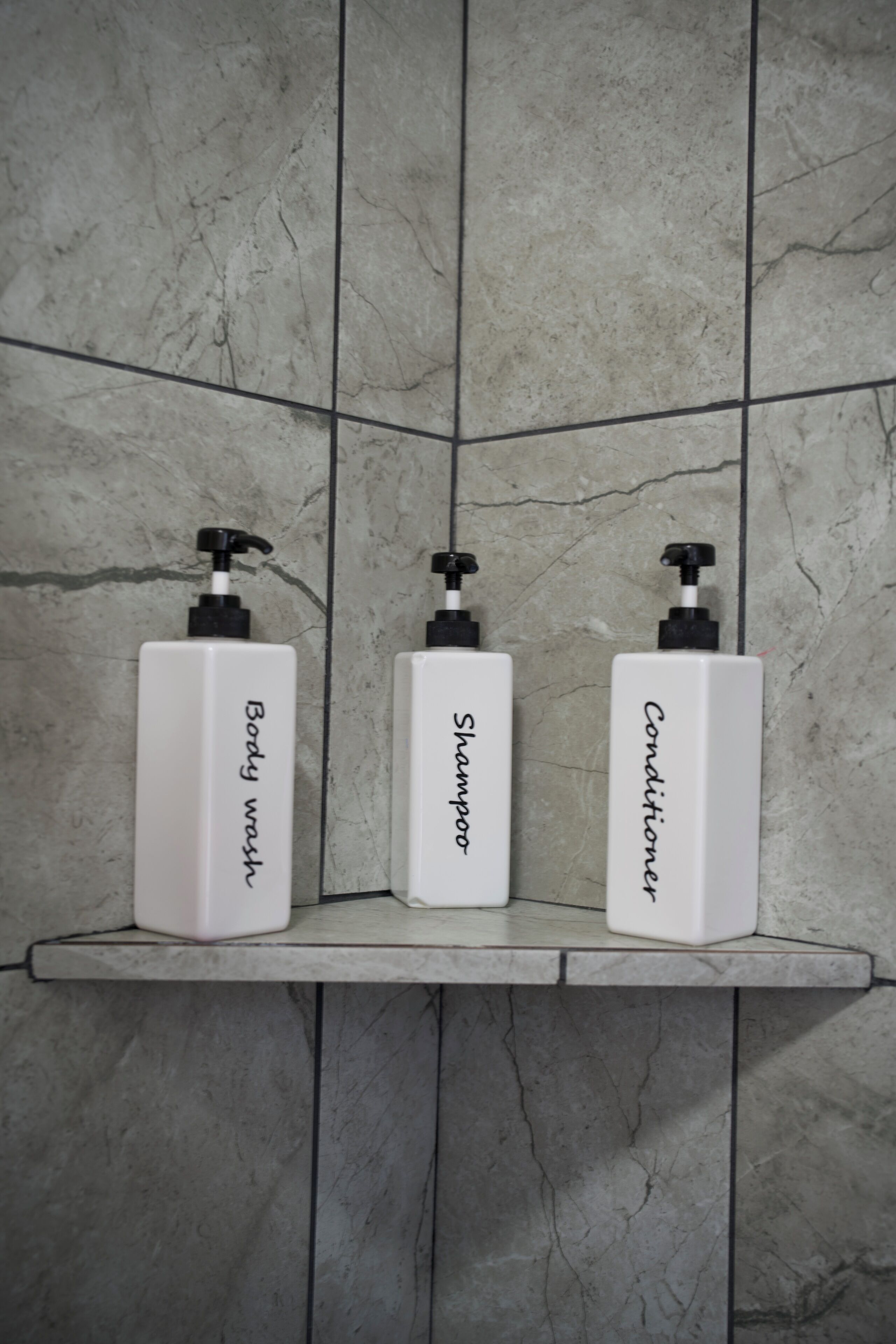 Three white bottles with black pumps on a tiled shelf.