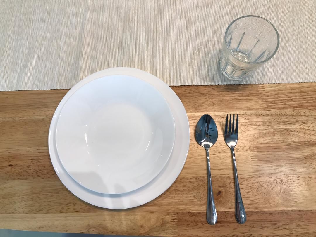Une table à manger avec une assiette blanche, un verre et des couverts en argent.