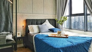 A bedroom with a bed, a bedside table, a dresser, a window with curtains, and a city view. - Arte Plus by Poly City (Kuala Lumpur)