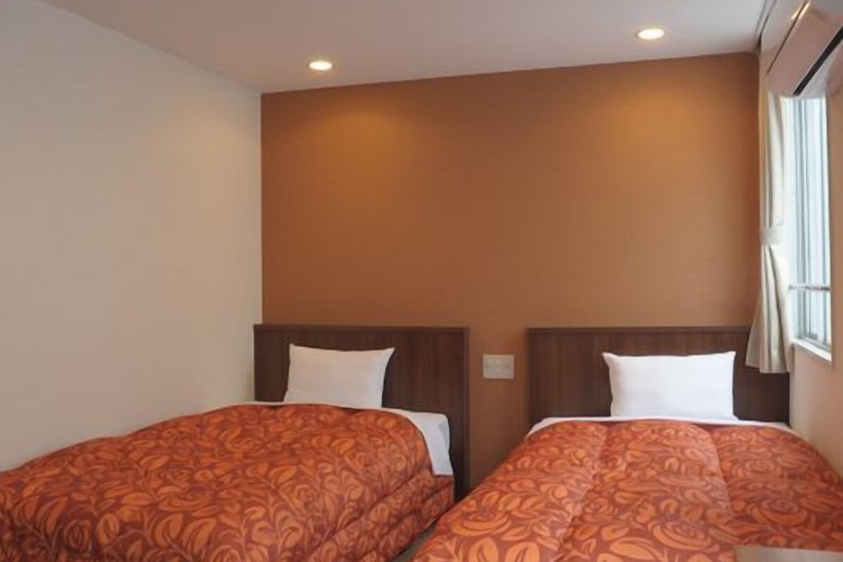 Een hotelkamer met twee bedden, elk met een beddengoed met een patroon, houten hoofdeinden en een raam met gordijnen.