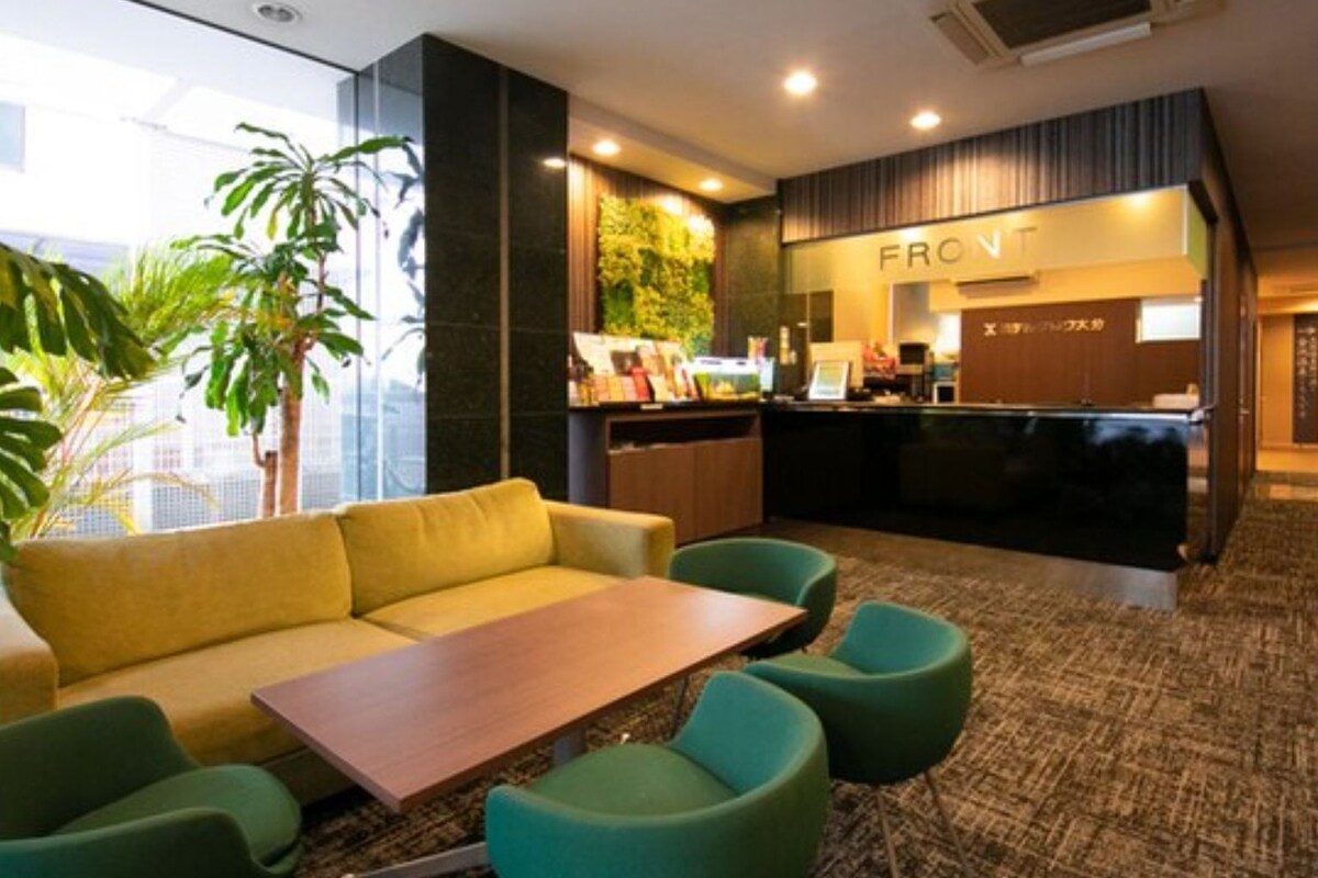 Een moderne hotellobby met een bank, stoelen, een houten tafel, een receptiebalie en een groene wand met planten.