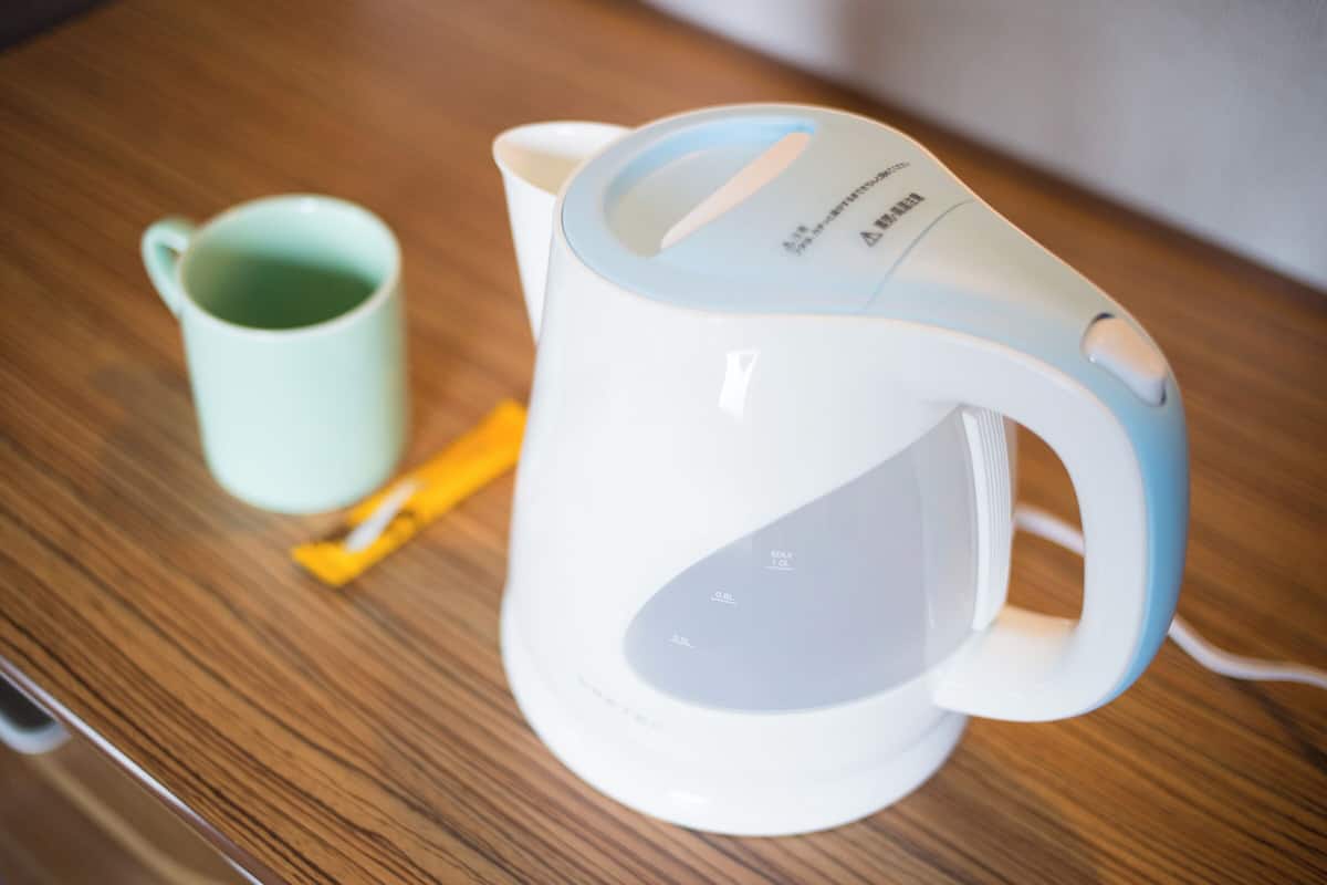 A white electric kettle with a blue handle and a green mug on a wooden table.