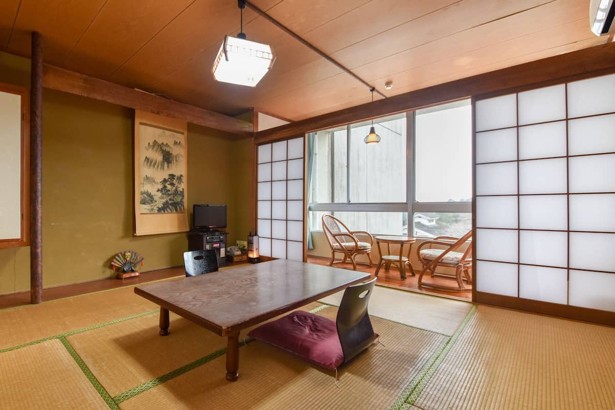 Una habitación japonesa tradicional con suelo de tatami, una mesa baja, un televisor y puertas correderas.