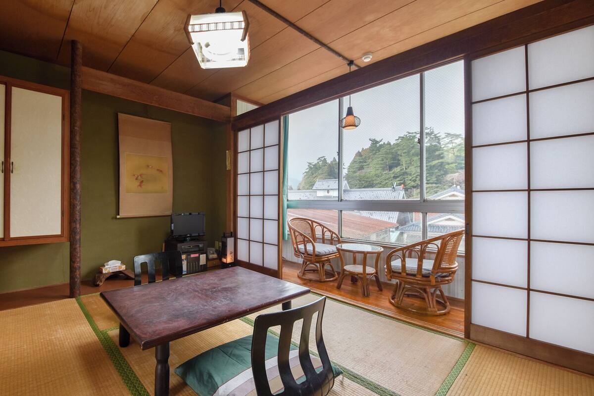 Una habitación tradicional japonesa con suelo de tatami, una mesa de madera baja y vistas a través de puertas shoji.