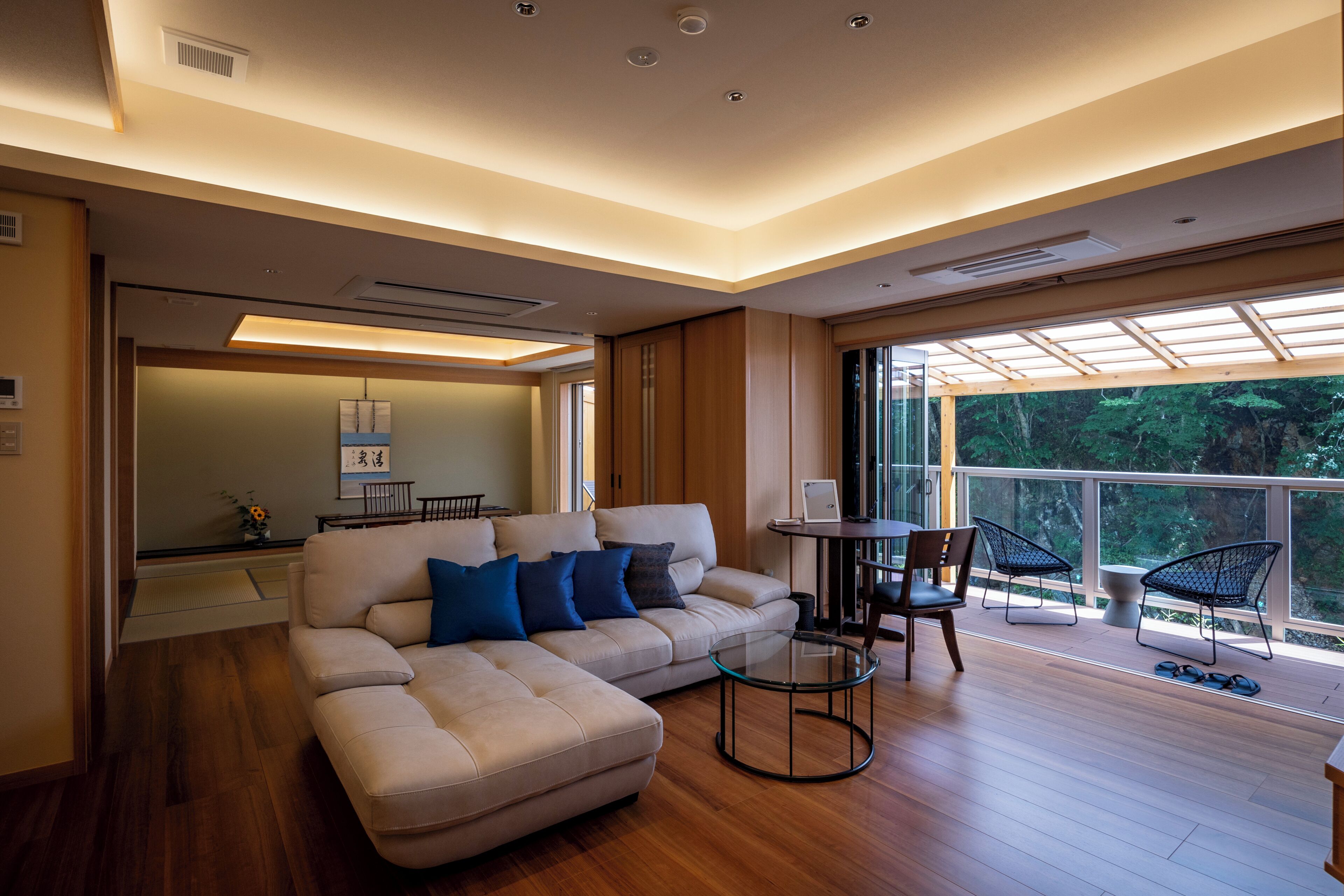 A modern living room with a sofa, a glass coffee table, and a dining area with chairs.