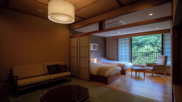 A traditional Japanese-style room with tatami flooring, a low wooden bed, a sofa, a table, and a sliding shoji screen. - Yunohanaso (Nasushiobara)