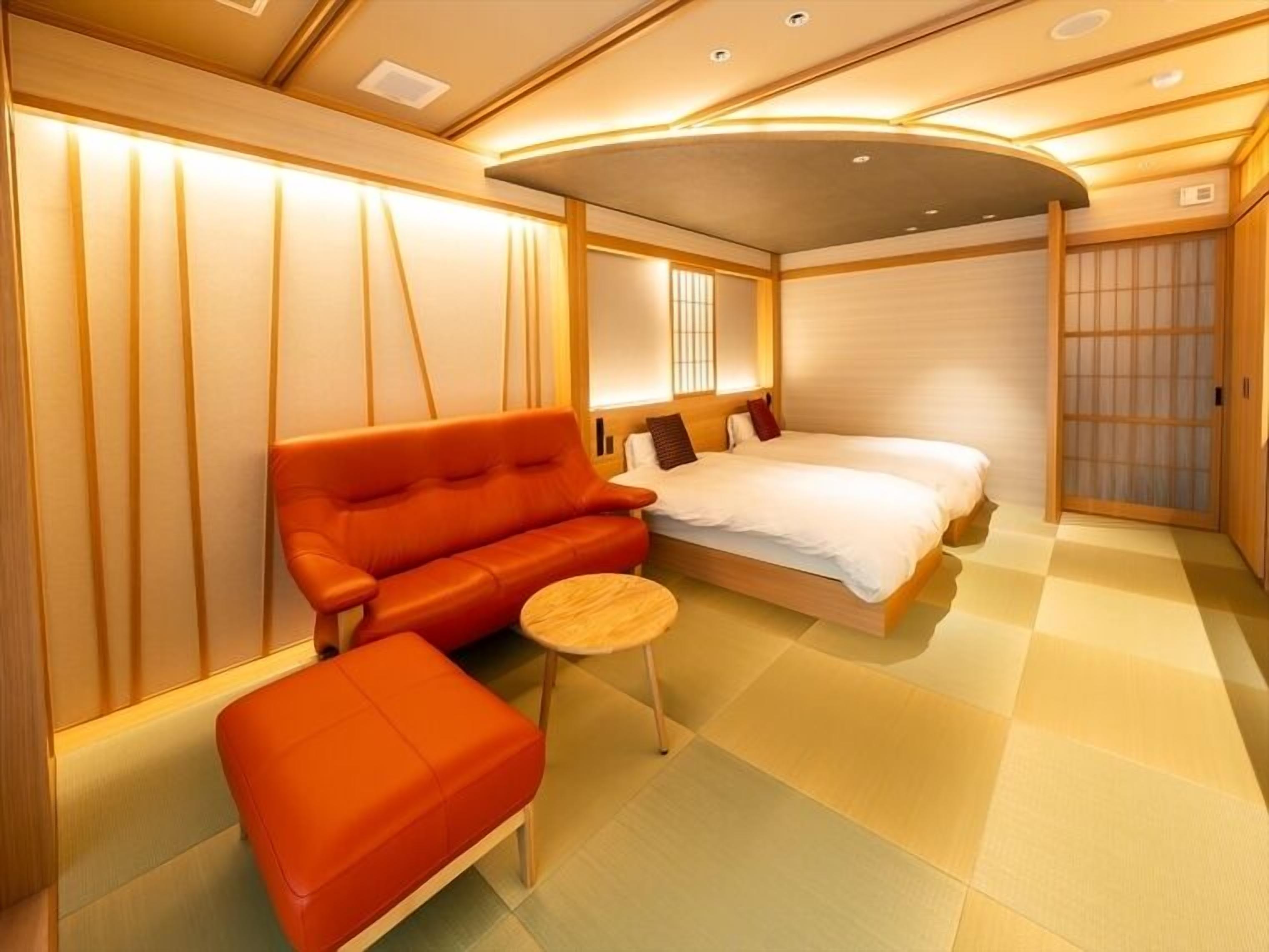A modern hotel room with a sofa, a bed, a small table, and a sliding door.