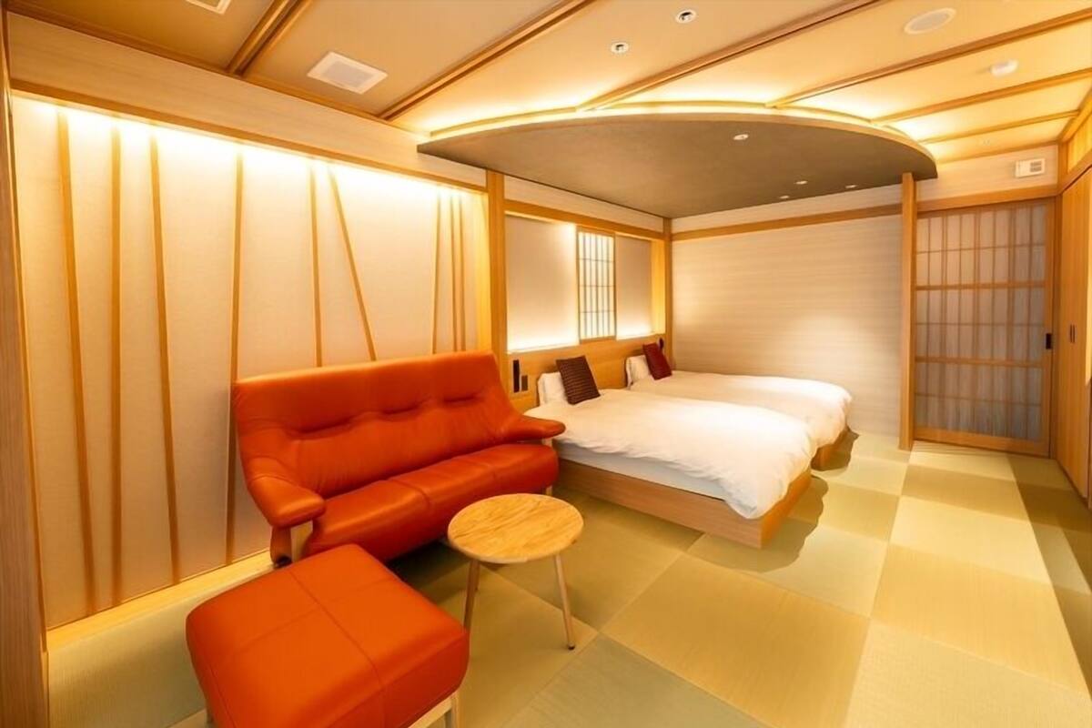 A modern hotel room with a sofa, a bed, a small table, and a sliding door.