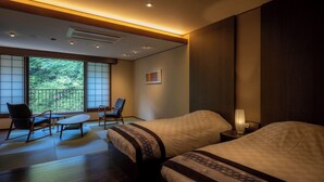 A hotel room with two beds, a sitting area with chairs, a large window with a view of greenery, and a wall-mounted air conditioner. - Yunohanaso (Nasushiobara)