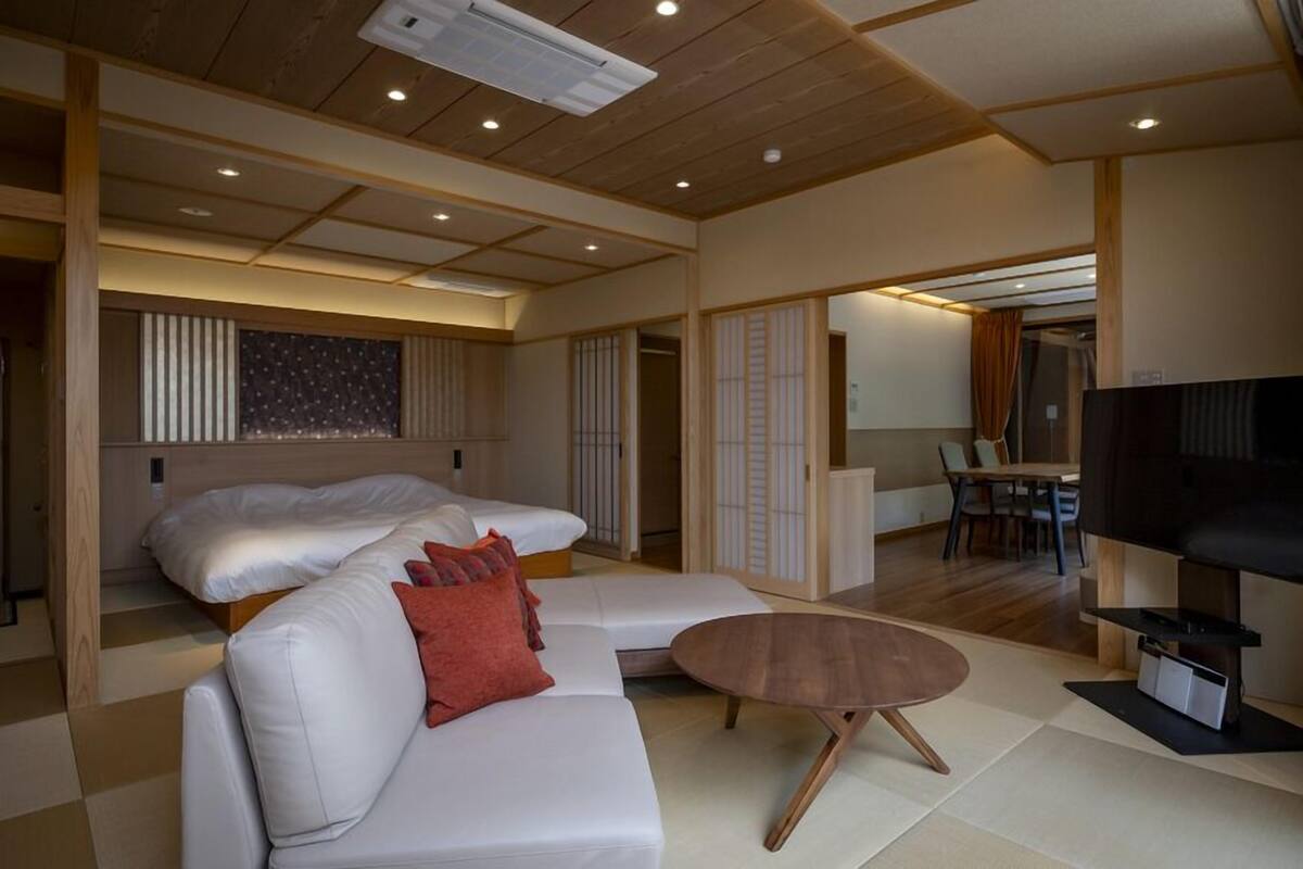 A modern hotel room with a sofa, a small coffee table, a TV, and a wooden ceiling.
