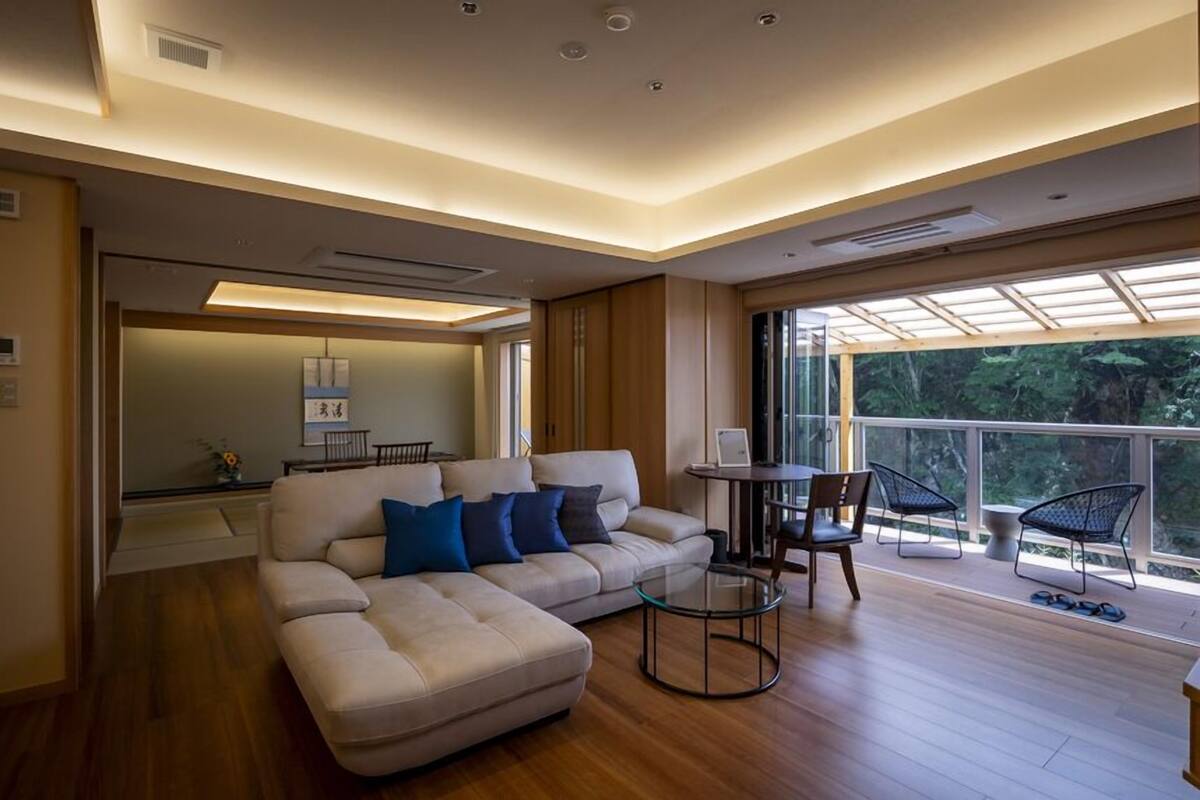A modern living room with a sofa, a glass coffee table, and a balcony with chairs.