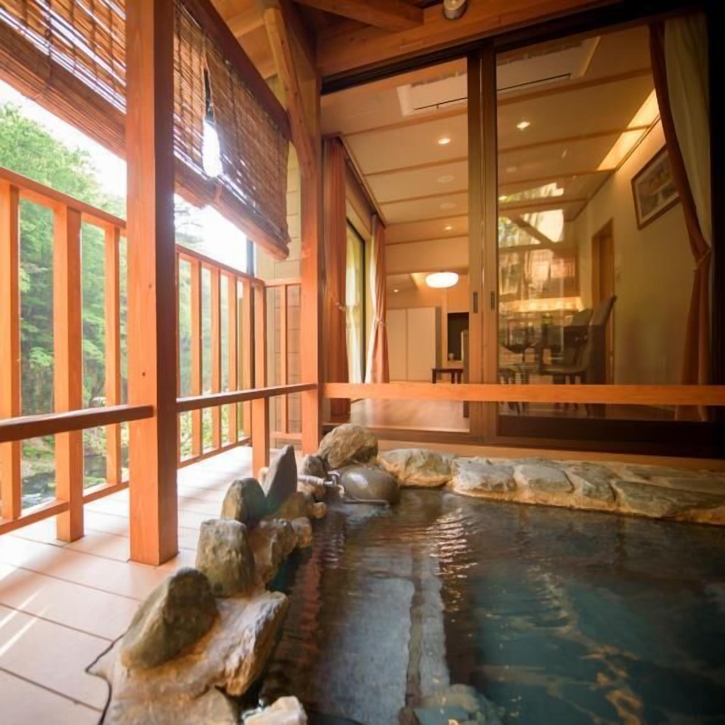 A traditional Japanese onsen with a wooden deck, stone seating, and a view of the surrounding forest.