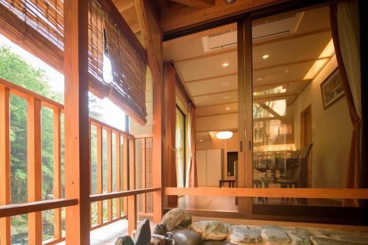 A traditional Japanese onsen with a wooden deck, stone seating, and a view of the surrounding forest.