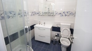 A modern bathroom with a glass shower enclosure, a white sink, a toilet, and a vanity with drawers. - Luxury apartment INA (Omis)