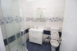 A modern bathroom with a glass shower enclosure, a white sink, a toilet, and a vanity with drawers.