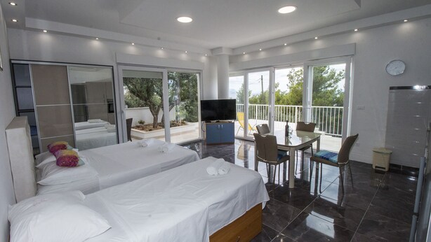 A modern hotel room with a large bed, a TV, a balcony with a table and chairs, and a view of the outdoors. - Luxury apartment INA (Omis)