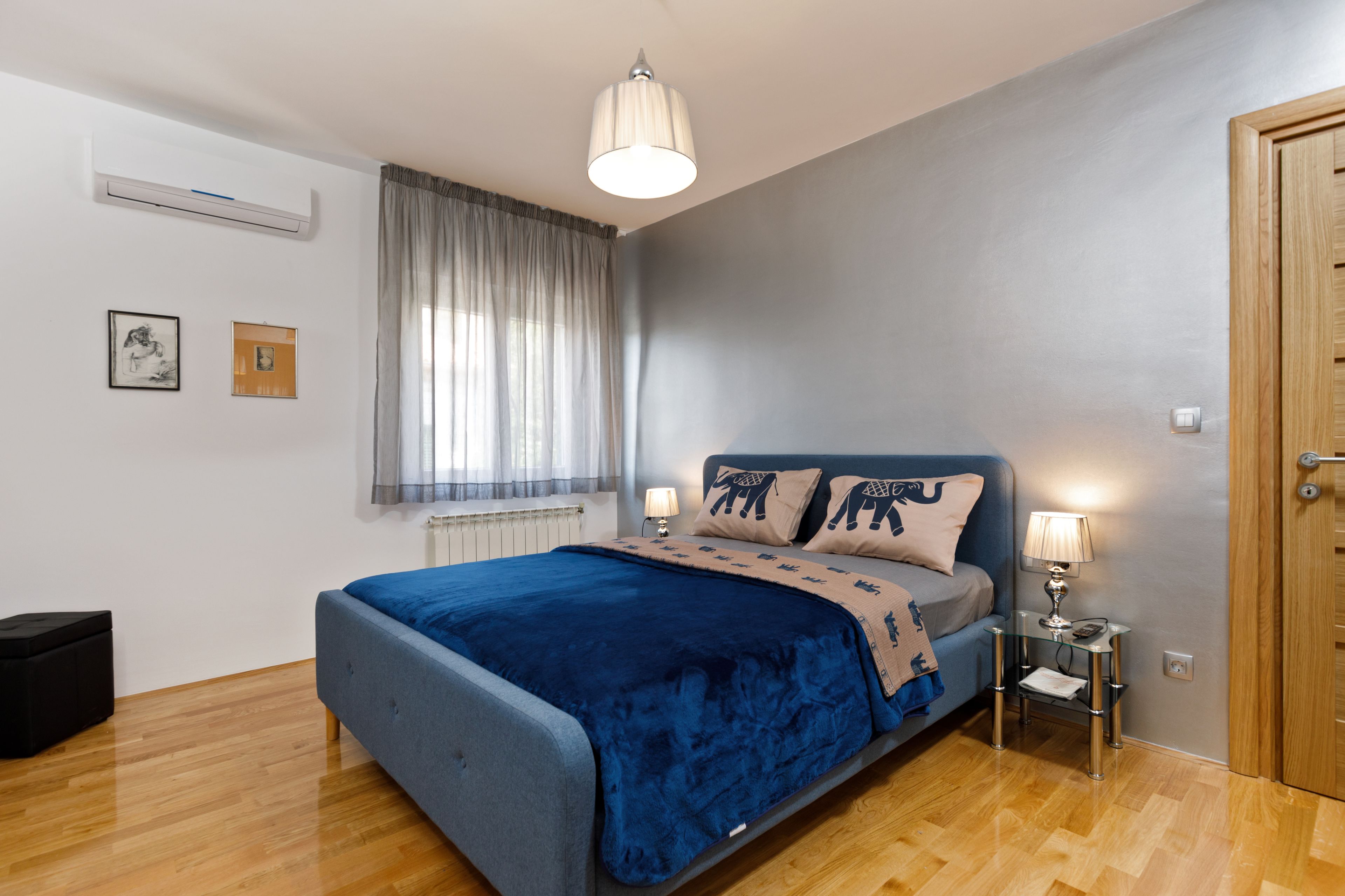 A bedroom with a bed, a bedside table with a lamp, a window with curtains, and a radiator.