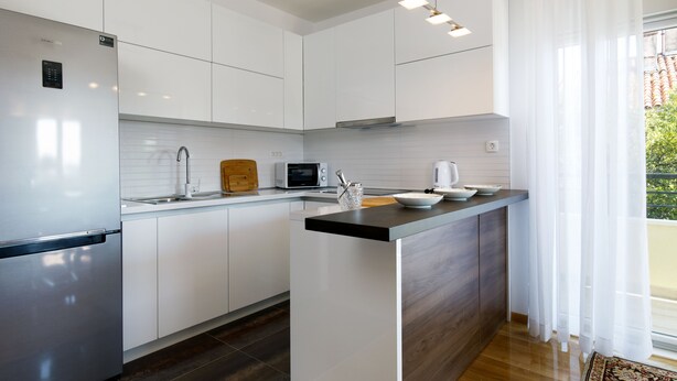 A modern kitchen with white cabinetry, a stainless steel refrigerator, a microwave, and a wooden cutting board. - Luxury beach apartment private parking (Split)