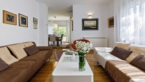 A modern living room with a brown sofa, a white coffee table, and a vase of flowers. There is a dining area in the background with a table and chairs. - Luxury beach apartment private parking (Split)