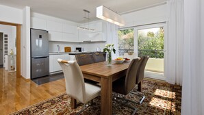 A modern kitchen with white cabinets, a stainless steel refrigerator, and a dining area with a wooden table and chairs. - Luxury beach apartment private parking (Split)